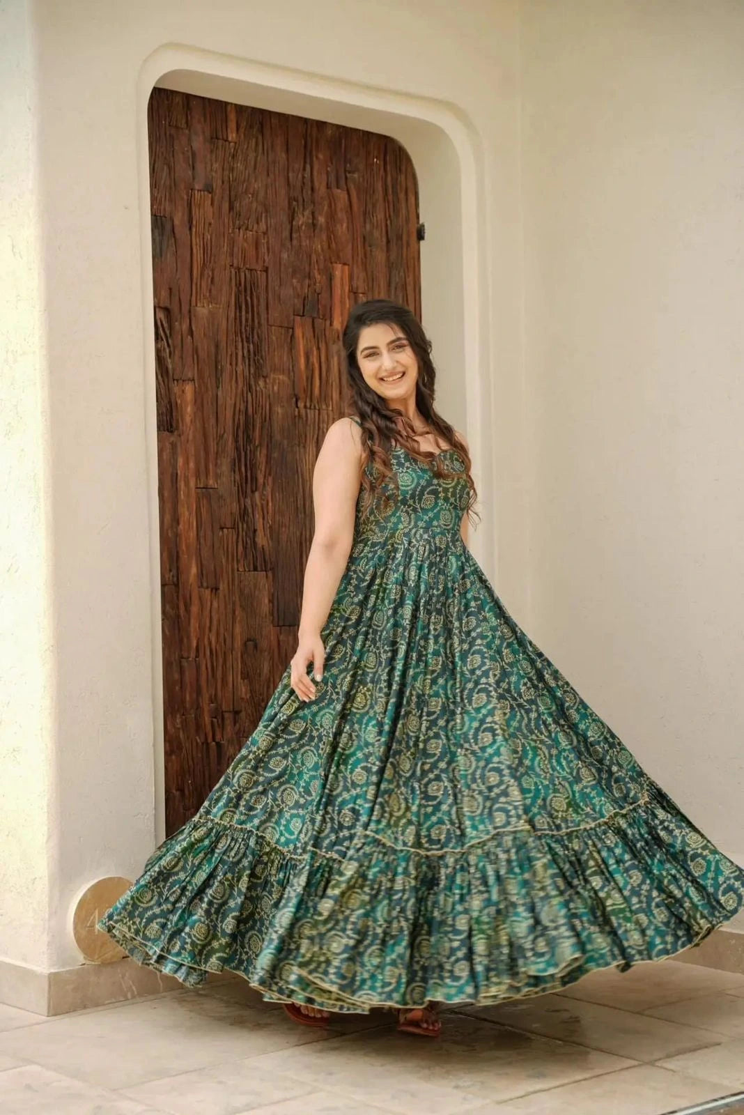 Woman in a green patterned dress standing in front of a wooden door.
